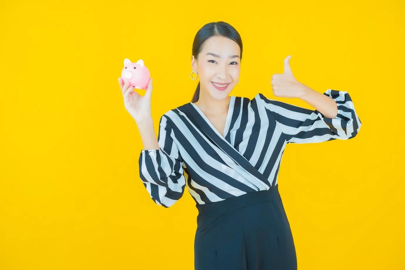 Porträt einer schönen jungen asiatischen Frau mit einem Sparschwein vor gelbem Hintergrund